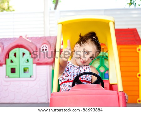 children girl driving a toy car with ok hand gesture in playground