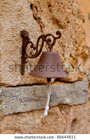 Aged rusty iron little bell hanging from stone wall in Majorca