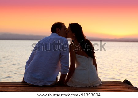 couple kissing at sunset sitting in jetty at orange sea lake