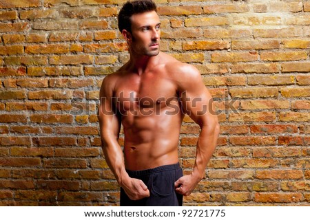 muscle shaped man posing on gym grunge brick wall