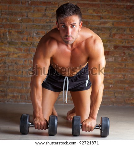 muscle shaped man on knees with training weights on brick wall