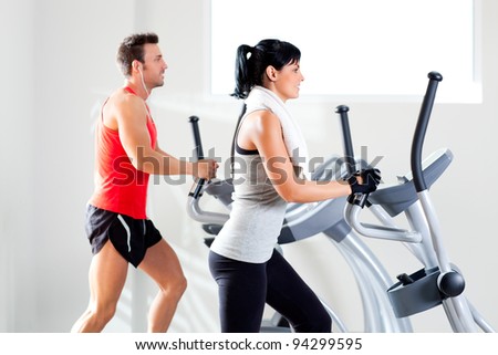 man and woman with elliptical cross trainer in sport fitness gym club