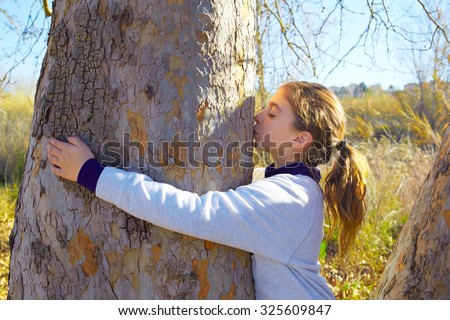 Kid girls loves nature hug and kiss a tree trunk in outdoor winter park