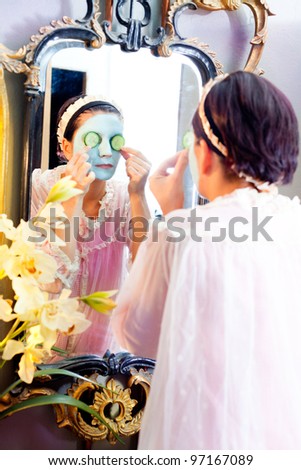 Funny housewife beauty green clay mask and cucumber at the mirror