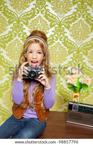 hip retro little girl shooting photo with vintage camera on wallpaper