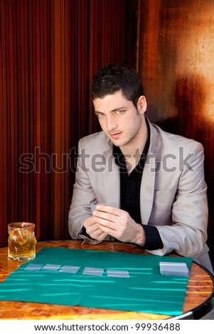 Latin handsome gambler man in table playing poker cards and drinking whiskey