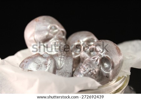 Four silver sprayed chocolate candy skulls in a glass bowl for halloween