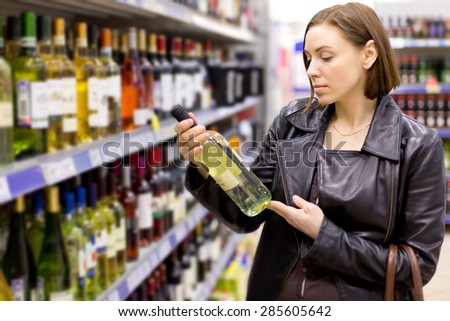 Young woman is choosing wine in the supermarket.