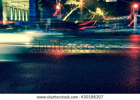Vintage style - Rainy night in the big city, light from the shop windows reflected on the road on which cars travel. View from the level of asphalt