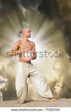 Man Practises Tai Chi holding a Ball of Energy with Dramatic Cloudy Sky and  Sun Rays in Background
