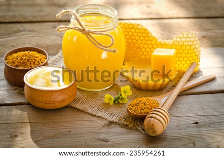 two wooden bowls one with honey another with pollen.The bank of honey stay near honeycombs,wax,wooden spoon with honey and dipper