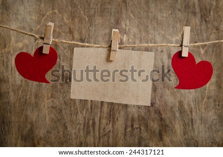 Two Red fabric hearts with sheet of paper hanging on the clothesline on three clothespins . On old wood background.