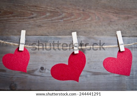 Three Red fabric hearts hanging on the clothesline on three clothespins . On old wood background.