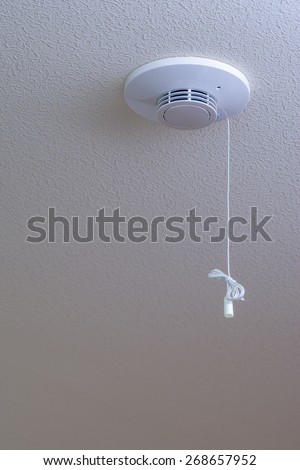 A white fire alarm on a textured white ceiling.