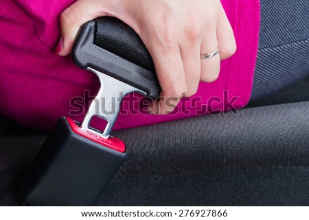 A girl wearing a pink shirt buckling a seatbelt