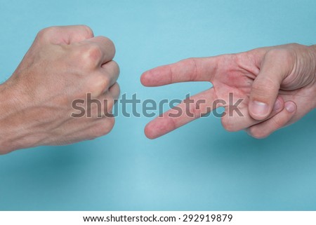Men\'s hands playing rock, paper, scissors on a light blue background. One is throwing rock, the other is throwing scissors.