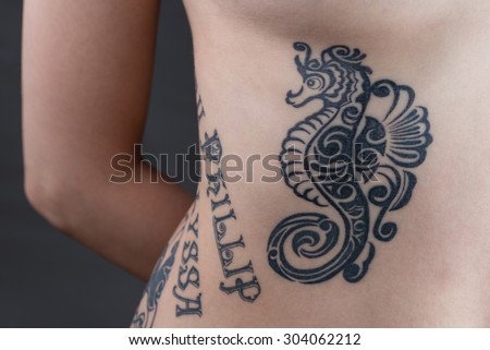 A tattoo of a black tribal style seahorse with children\'s names wrapping around a woman\'s ribs.