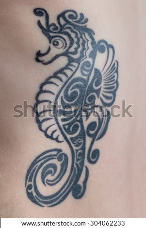 A tattoo of a black tribal style seahorse on a woman\'s ribs.