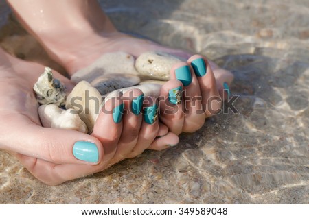 Woman hand with turquoise nail design and sea stones. Clean sea water.