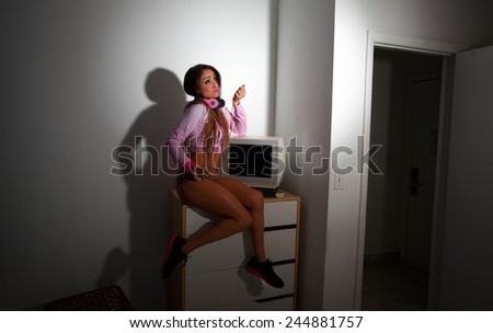 Young Pretty Latino Woman sitting in a hotel room lifting a vintage television set above her head