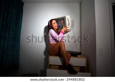 Young Pretty Latino Woman sitting in a hotel room lifting a vintage television set above her head