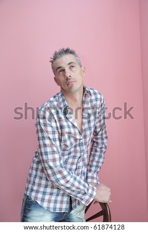 man in a checked shirt leaning against a chair