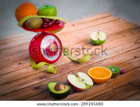 a series of fruit placed on a balance of weight, with a tape measure and on a wooden board