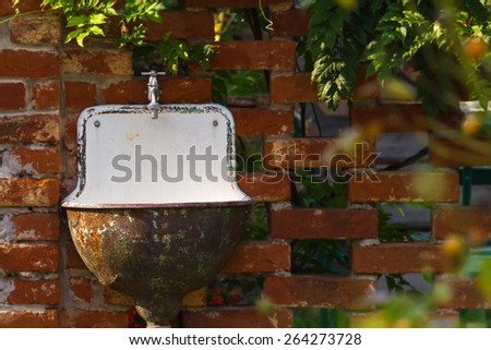 Old garden sink on a brick wall surrounded by leafs