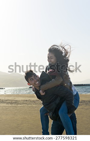 Hispanic and Japanese Couple looking at each other lovingly at the beach wearing jackets and scarfs as the wind blows
