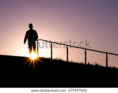 Silhouette of a man on top or a staircase outdoors with the sun between his legs during Sunset