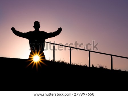 Silhouette of a man with arm up in the air on top of a staircase outdoors with arms in the air during Sunset
