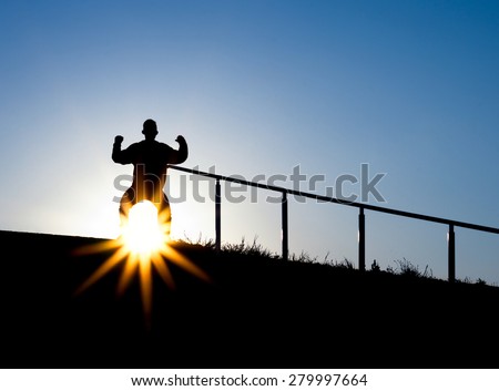 Silhouette of a man with arm up in the air on top of a staircase outdoors with arms in the air during the day