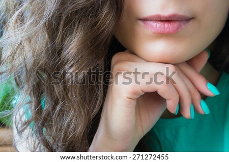 young beautiful girl with brown shiny hair holds a hand with a turquoise nail polish near the chin, lips dyed red lipstick. the image is dominated by green, the model\'s face is not visible