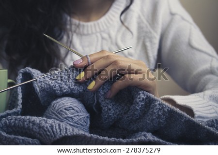 In the center of the image of a young girl\'s hand with bright manicure keeps knitting with spokes. The girl wearing a white sweater. Vintage photo. Close-up.