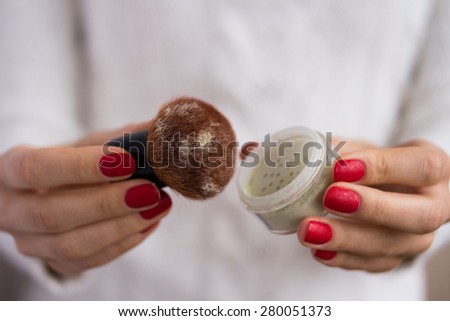 Brush and powder in female hands with red nails.