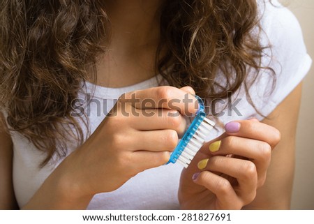 Treatment of the nails with a brush. Hands of a young girl with a bright manicure keep cosmetic tool closeup.