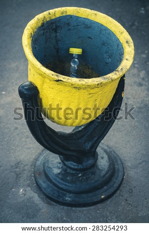 Black and yellow steel rubbish bin on the street close up. In the urn empty plastic bottle with yellow cap.