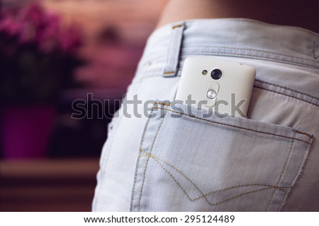 White mobile phone in the back pocket women\'s jeans on a purple background closeup.