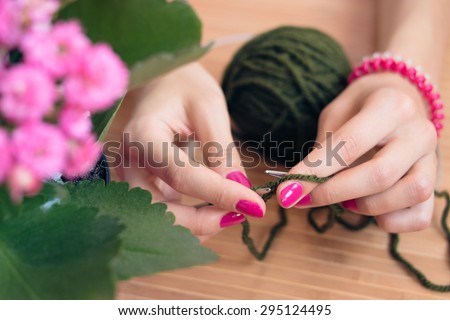 Women\'s hands with pink manicure knit metal spokes. Nearby is a pink flower in a pot. Knitting closeup.