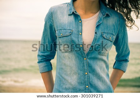 Denim shirt on a girl with curly hair close-up on a background of the sea. Bright retro colors.