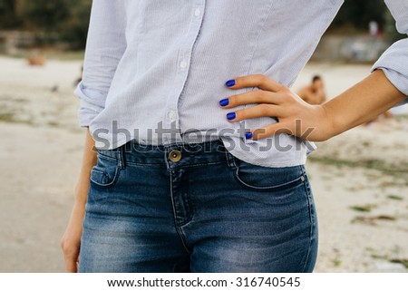 Details of women\'s clothing. The woman in jeans and shirt standing on the beach. Close-up, outdoors.
