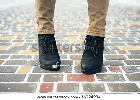 Female feet in an elegant black winter boots standing on snow-covered sidewalk in the winter, close-up