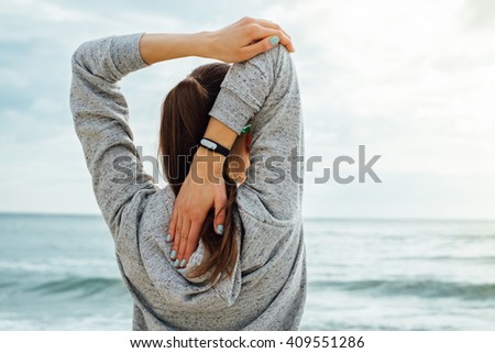 Girl in sportswear stretches the triceps in the early morning on the beach. View from the back.