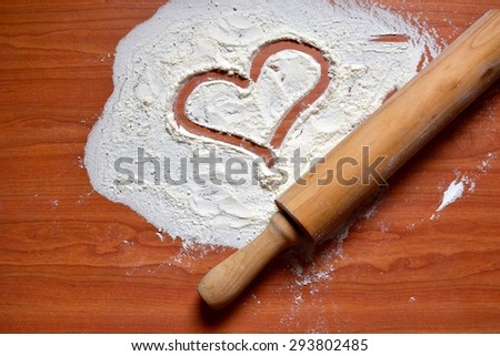 A heart drawn with flour and wooden dough roller on the brown wooden table background