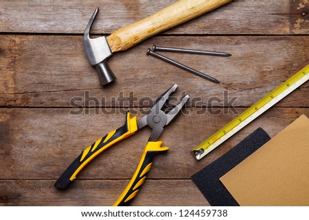 Construction instruments on wooden table - sandpaper, pliers, measuring tape, hammer, nails