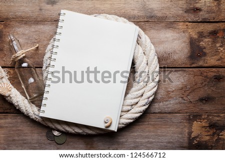 Blank open notebook on sea rope with bottle and ancient coins, on wooden table