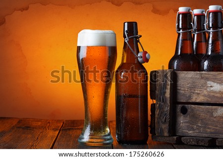 Beer glass with wooden crate full of beer bottles on table