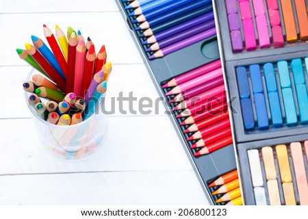 Multi colored pencils in jar on wooden table, with pastel and pencils box on background