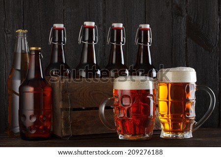 Beer glasses on table with crate full of bottles, dark wooden background