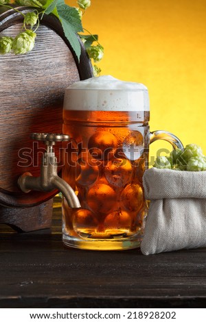 Wooden beer barrel with fresh hop cones and glass of beer on table close up